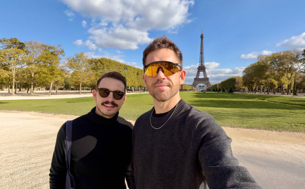 Andrew and Dylan standing in front of the Eiffel Tower in Paris, France on a sunny day at Champ de Mars