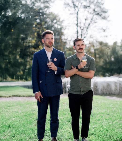 Andrew Curry and Dylan Cunningham holding champagne glasses outdoors at an outdoor celebration