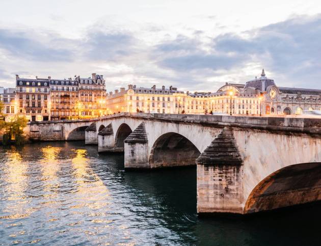 Seine River in Paris with historic stone bridge and Haussmann buildings along the riverbank at sunset